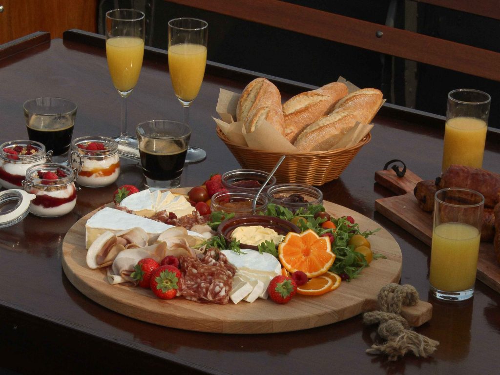 The Boat Café - Brunch & Breakfast boat with croissant, pain au chocolat, jam, butter, cheeses, ham and charuterie and breads, salads, granola bowls, coffee and juices